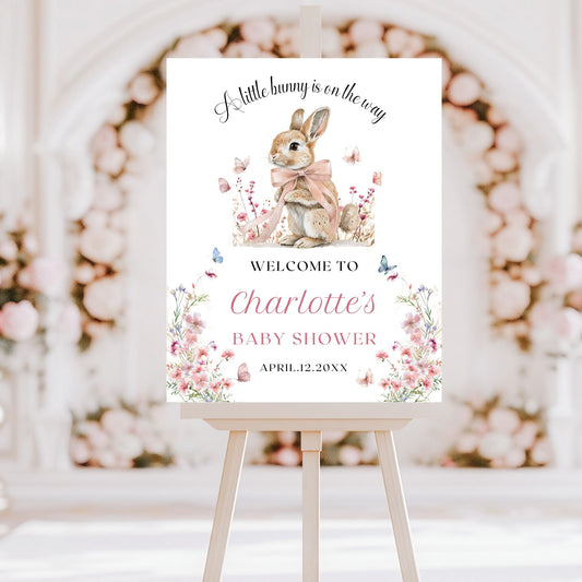 Baby shower invitation with a bunny illustration on an easel against a floral backdrop.