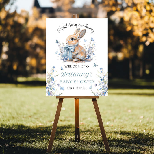 Baby shower welcome sign with a bunny illustration on an easel outdoors.