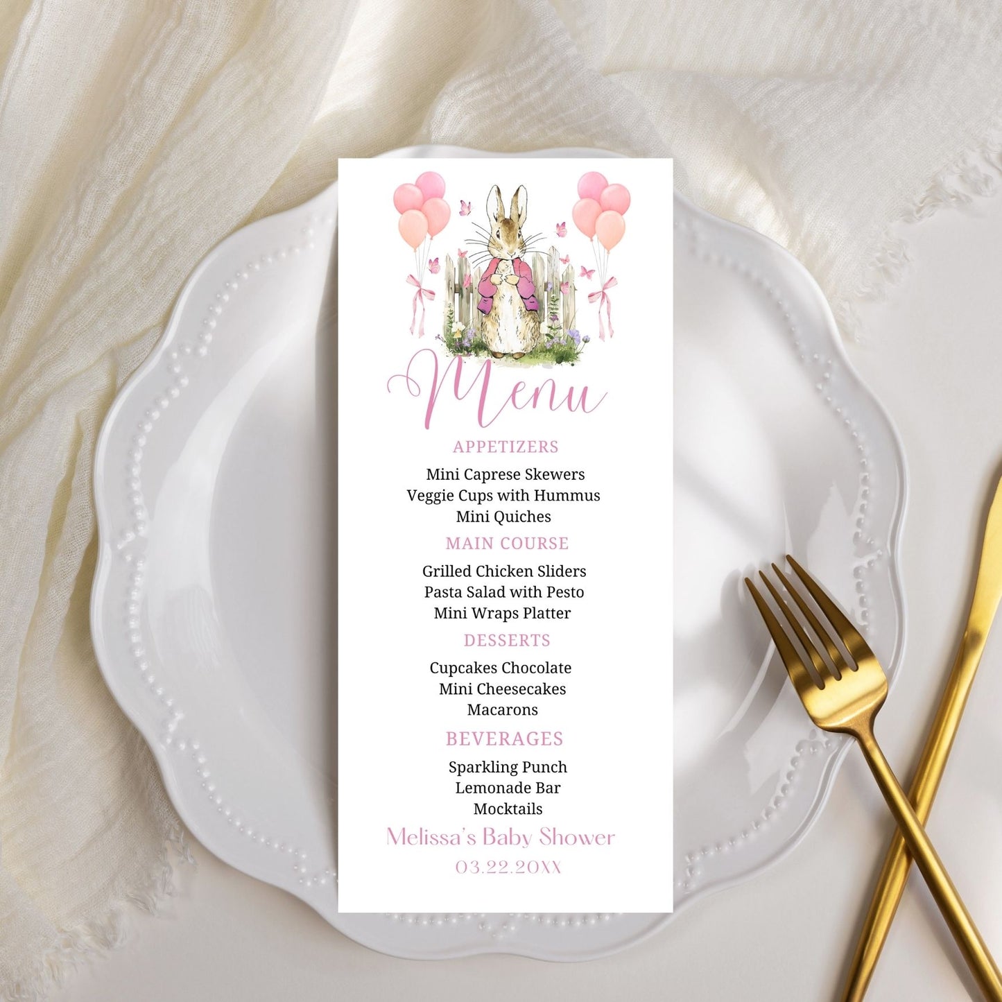 Menu card for a baby shower on a white plate with a gold fork, featuring a rabbit illustration and pink balloons.