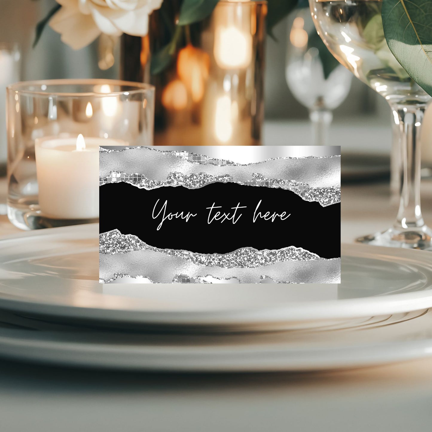 Decorative black and silver place card with text placeholder on a table setting with candles and glasses.