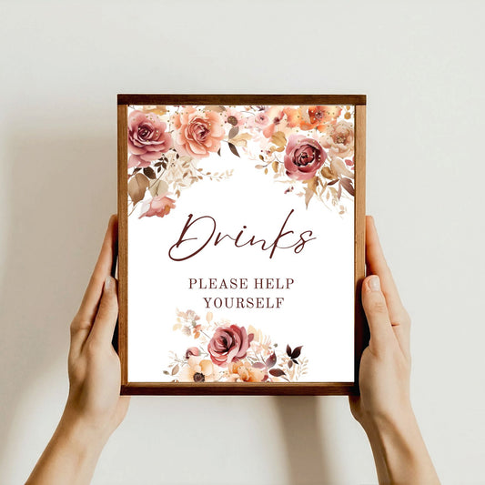 Framed Fall floral sign with 'Drinks Please Help Yourself' text held by hands against a light background