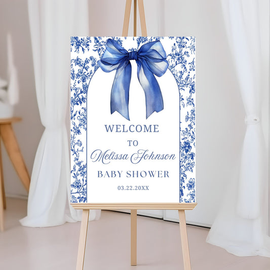 Baby shower welcome sign with blue bow and floral design on an easel.