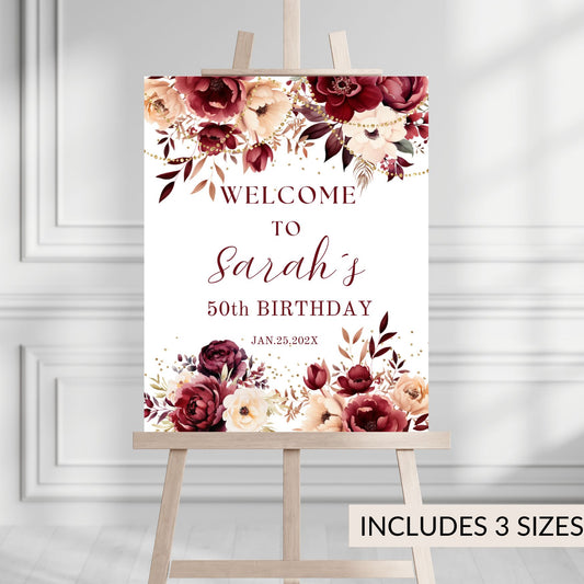 Burgundy Floral welcome sign for a 50th birthday celebration on an easel against a white wall.