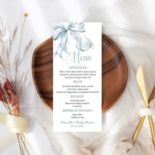 Menu card with decorative Dusty blue bow on a wooden plate with gold cutlery and floral decorations.