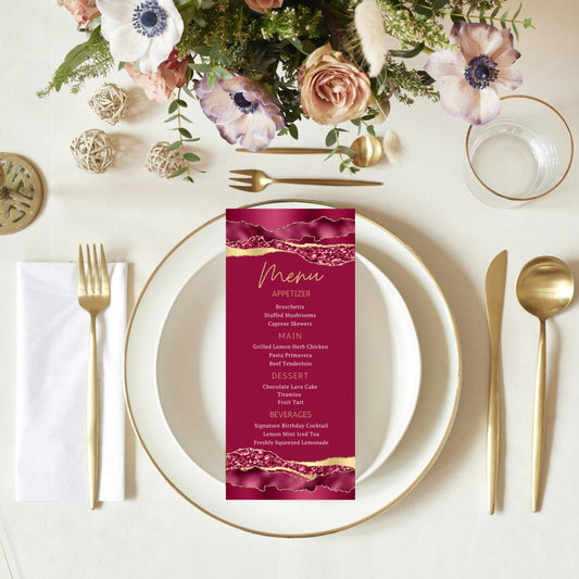 Table setting with a pink menu card, white plates, gold cutlery, and floral decorations.
