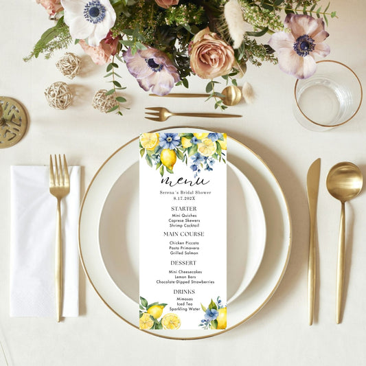 Table setting with blue floral menu card, plates, and cutlery on a white surface.