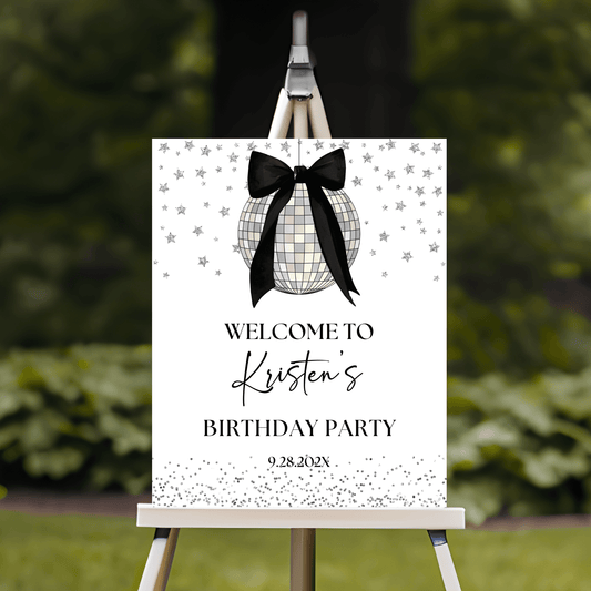 Coquette Black Bow Disco Ball Birthday Party Welcome Sign displayed on an easel in a garden setting.