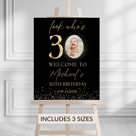Birthday sign with gold text and photo of a baby on a stand against a gray background