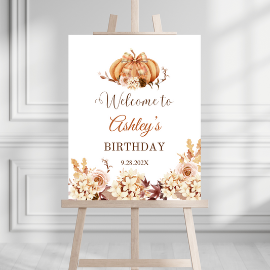 Editable Autumn Birthday welcome sign with pumpkins and floral decorations on a stand against a gray wall.