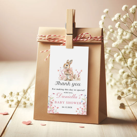 Kraft paper gift bag with a baby shower thank you card featuring a bunny illustration, tied with red and white string on a wooden surface.