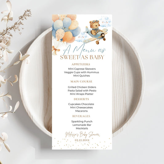 Baby shower menu card with teddy bear and balloons design on a white plate.