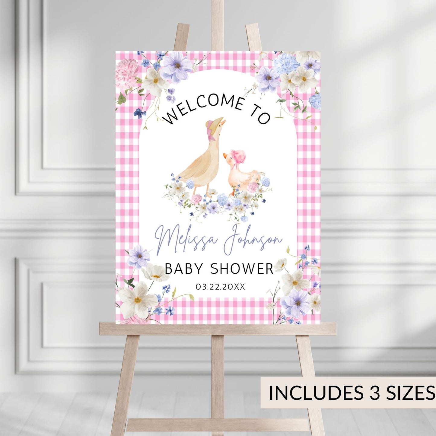 Baby shower welcome sign with floral design and text on a pink checkered background, displayed on an easel.