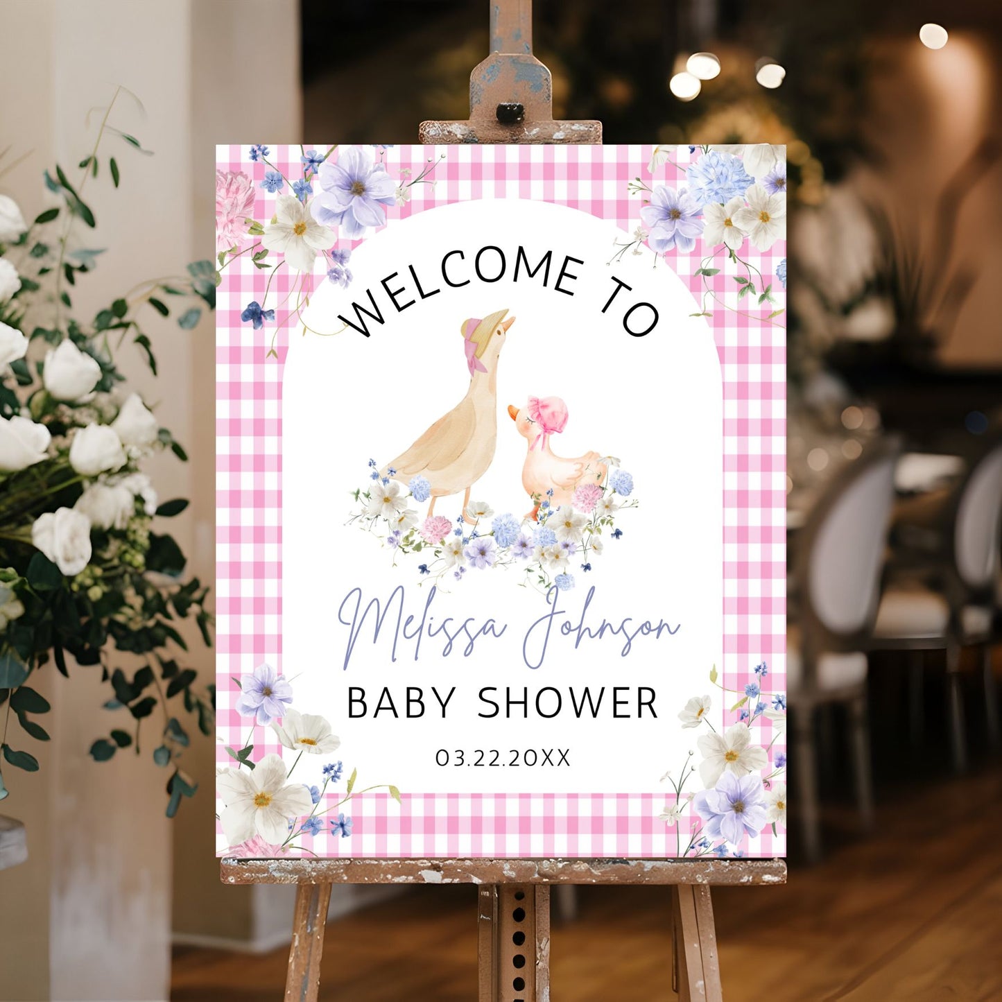 Baby shower welcome sign with floral design and checkered border on an easel.