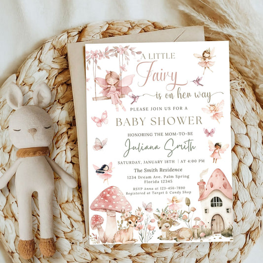 Fairy-themed baby shower invitation on a woven surface with a plush toy.