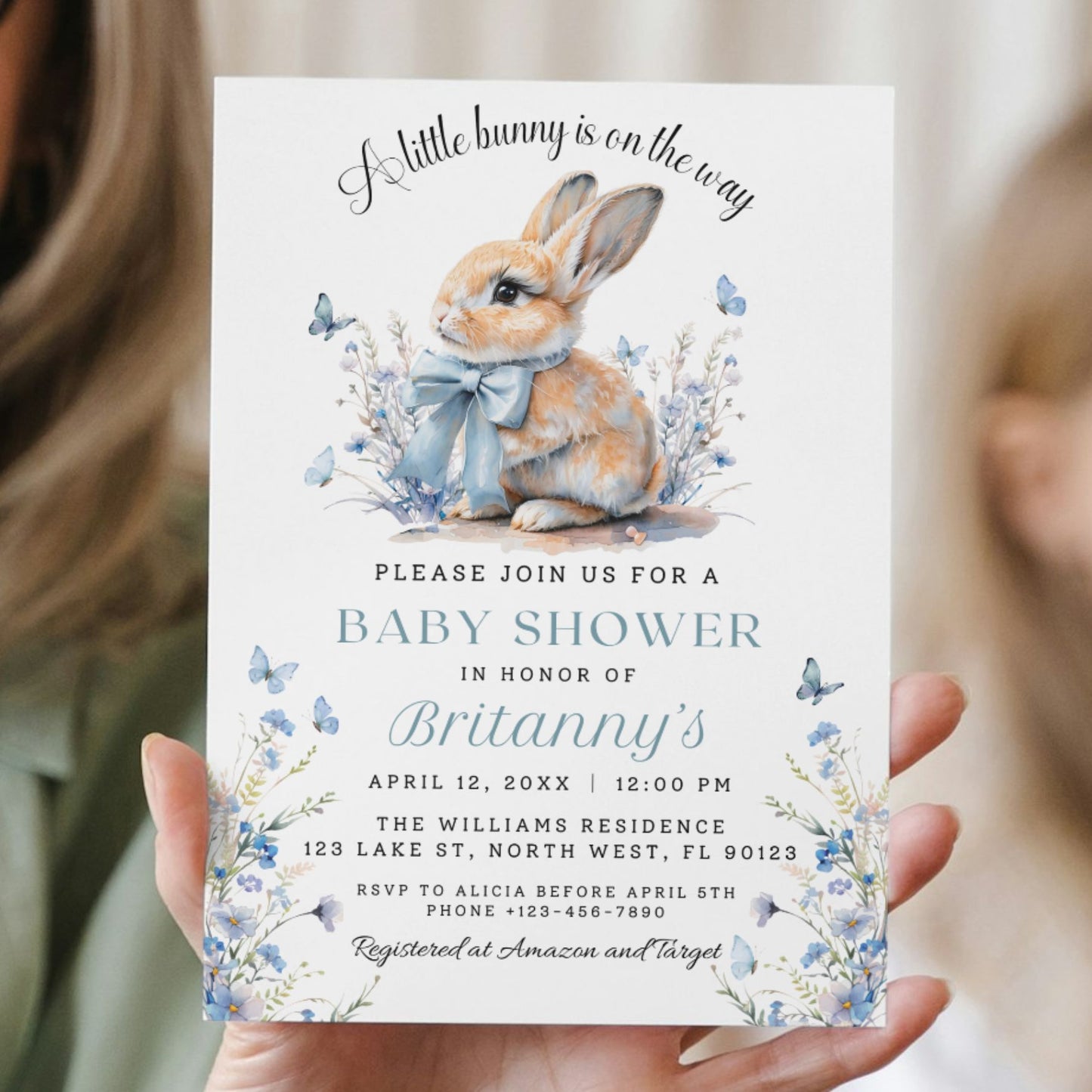 Baby shower invitation with a rabbit illustration held by two people.