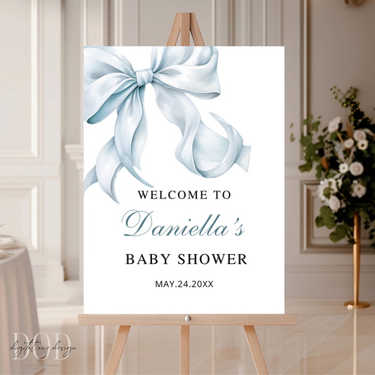 Baby shower welcome sign with a blue bow on an easel in a room setting.