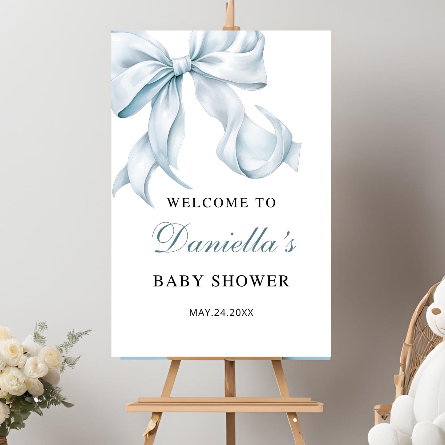 Baby shower welcome sign with a blue bow on an easel against a gray background