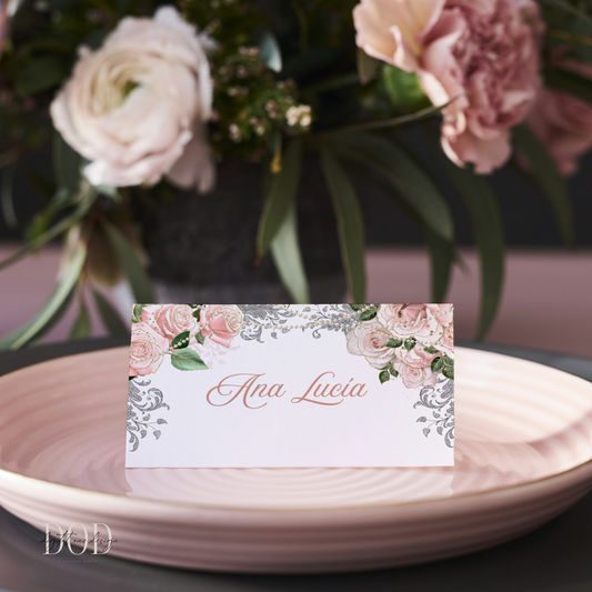 Rose Gold Floral and pearls place card on a pink plate with a blurred bouquet in the background