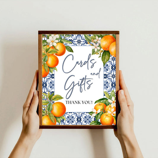 Framed artwork with Mediterranean oranges and floral design held by hands against a plain background