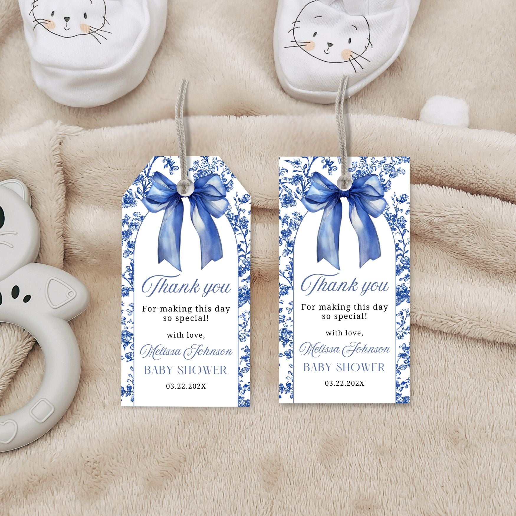 Two baby shower thank you tags with blue ribbons on a soft beige background.