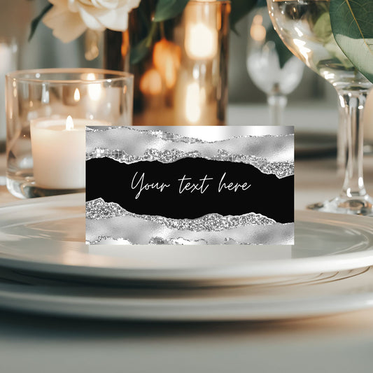 Decorative black and silver place card with text placeholder on a table setting with candles and glasses.