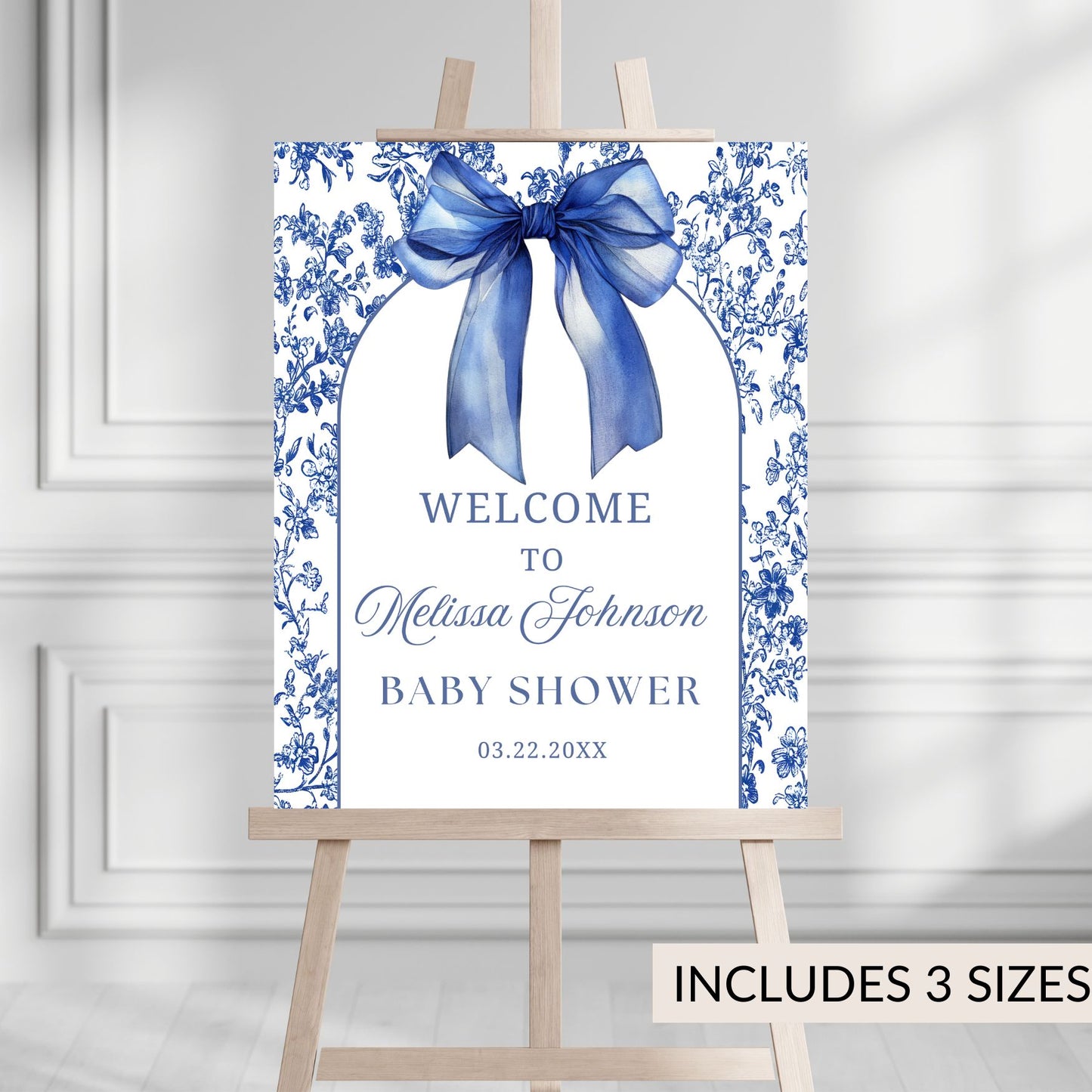 Baby shower welcome sign with blue bow and floral design on a white background, displayed on an easel.