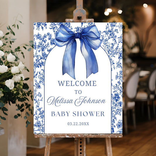 Baby shower welcome sign with blue bow and floral design on an easel.