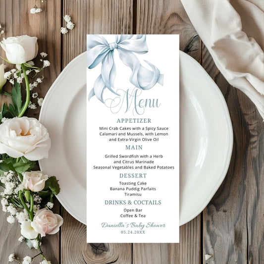 Dusty Blue Menu card for a baby shower on a wooden table with flowers and a white plate.