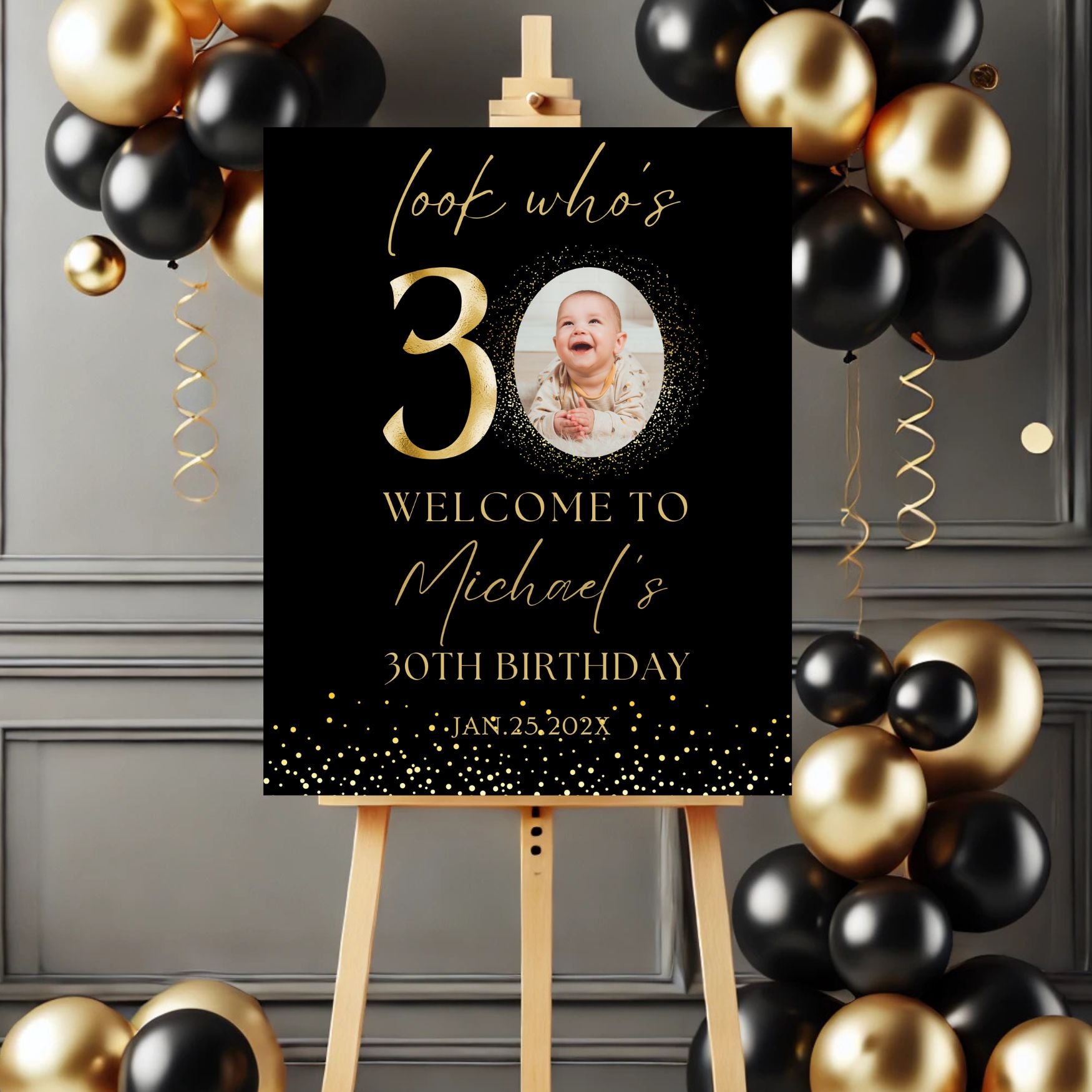 Gold Birthday sign with balloons on a stand against a gray wall