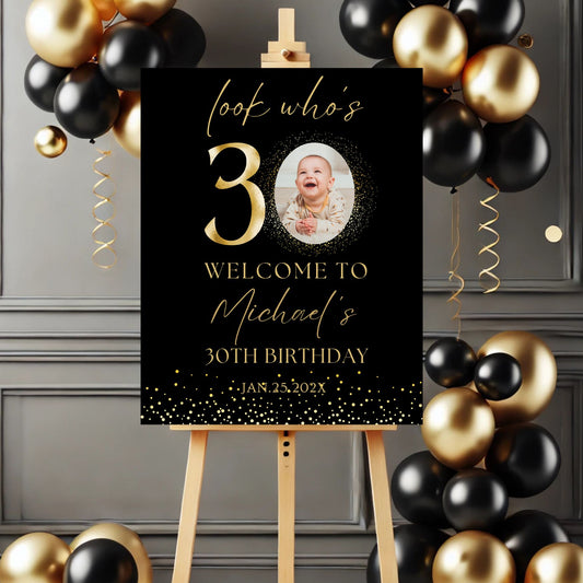 Gold Birthday sign with balloons on a stand against a gray wall