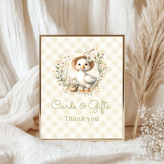Framed card with a baby goose and floral elements on a soft fabric background.