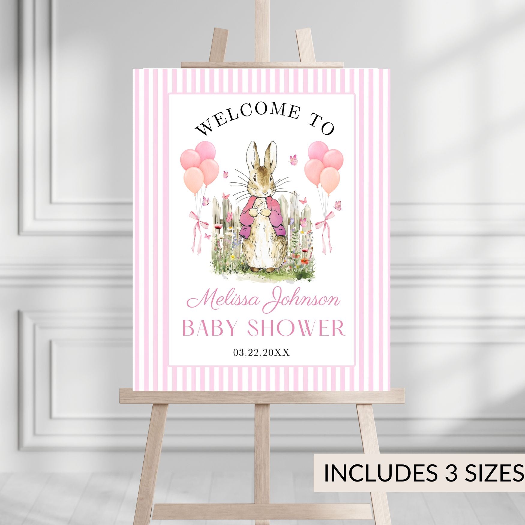 Baby shower poster with a Peter rabbit illustration on a pink and white striped background, displayed on an easel.