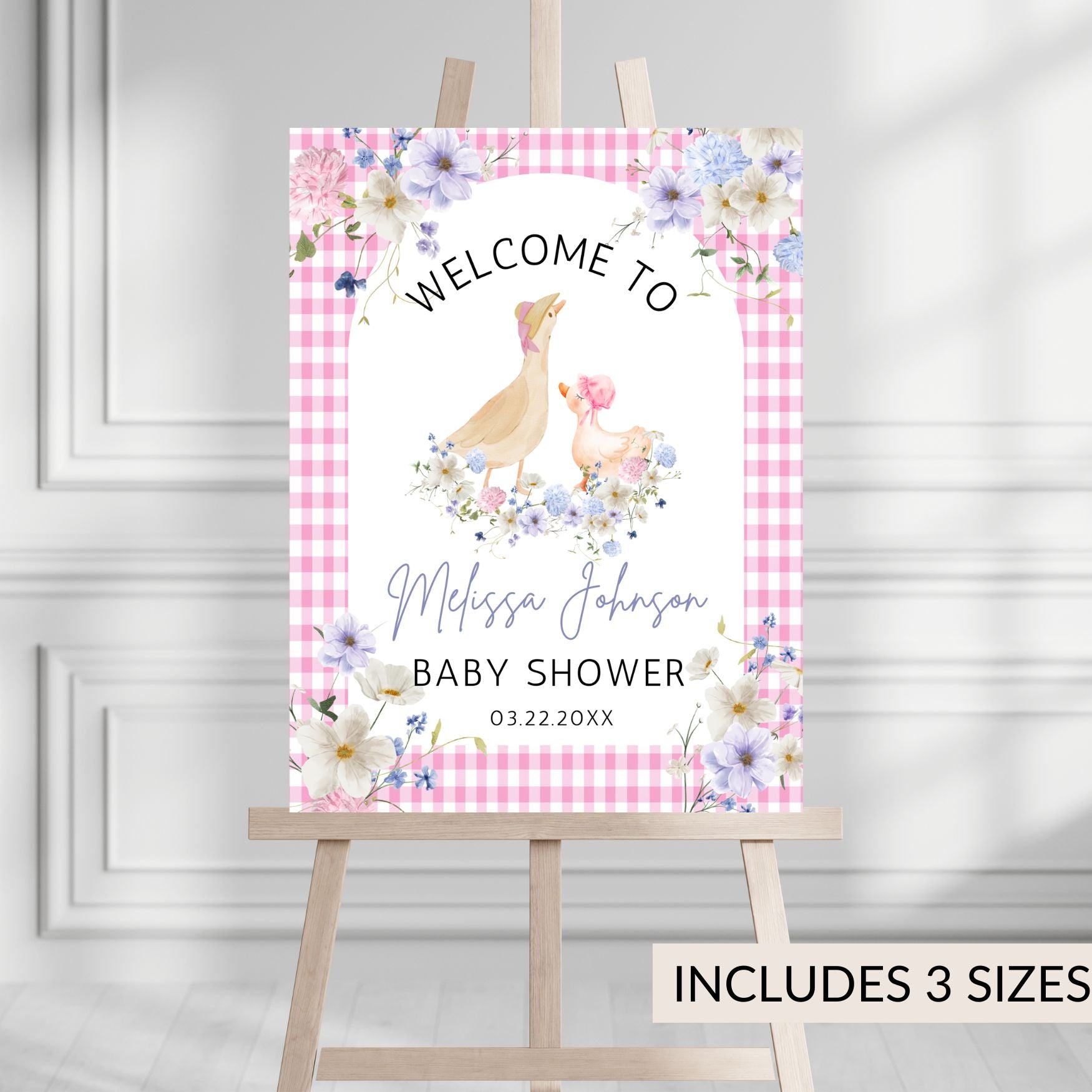 Baby shower welcome sign with floral design and text on a pink checkered background, displayed on an easel.