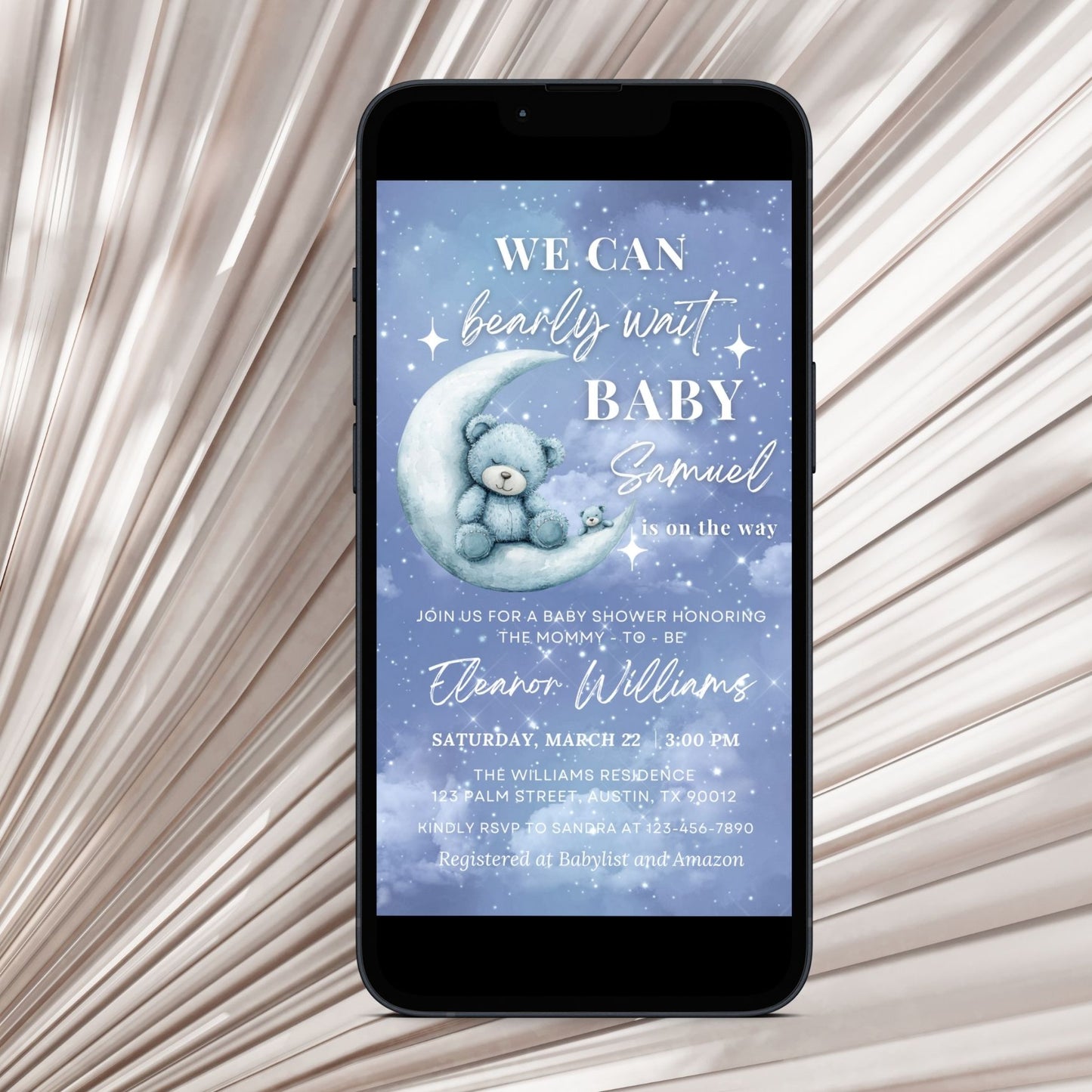 Phone displaying a baby shower invitation with a Cute teddy bear on a moon, on a textured beige background.