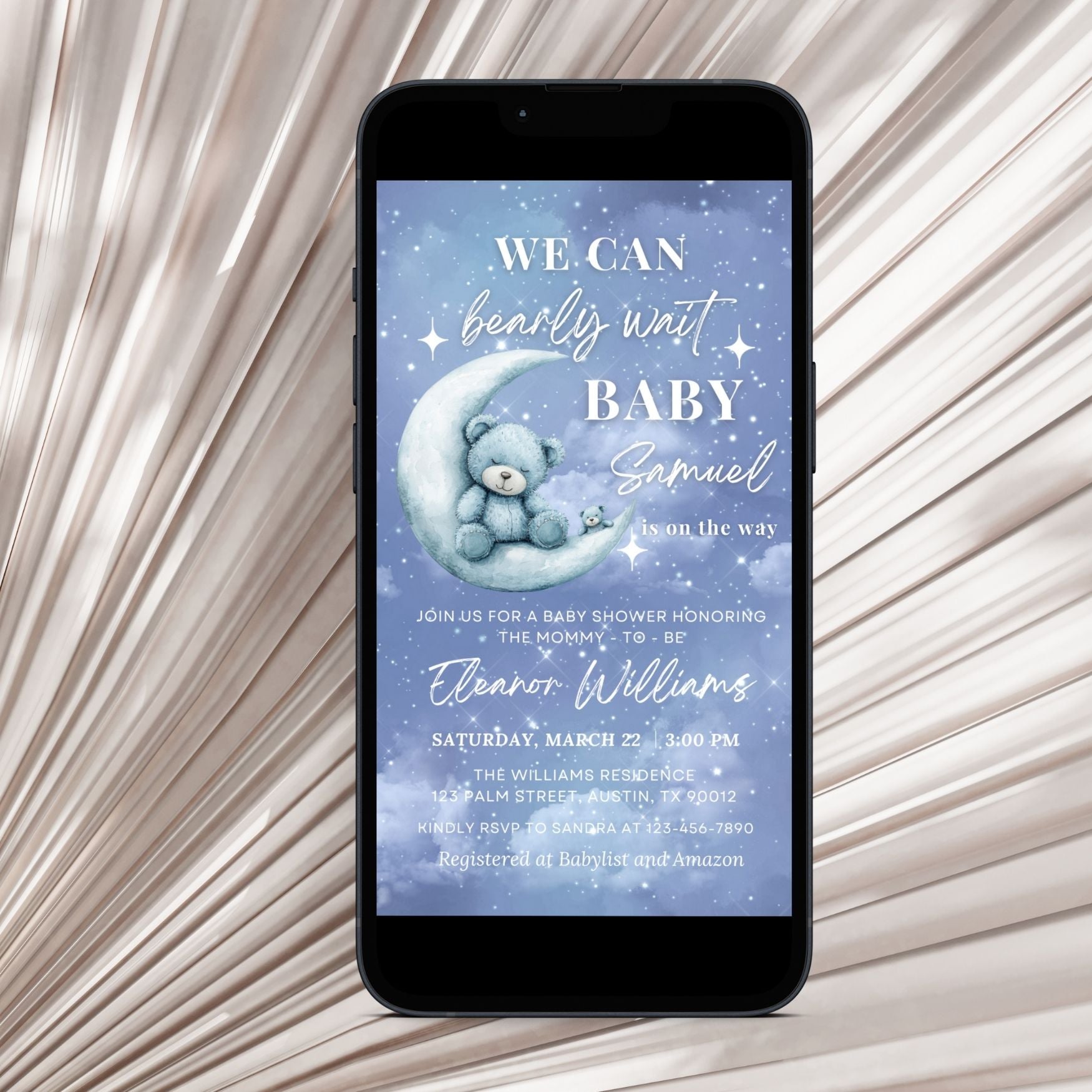 Phone displaying a baby shower invitation with a Cute teddy bear on a moon, on a textured beige background.