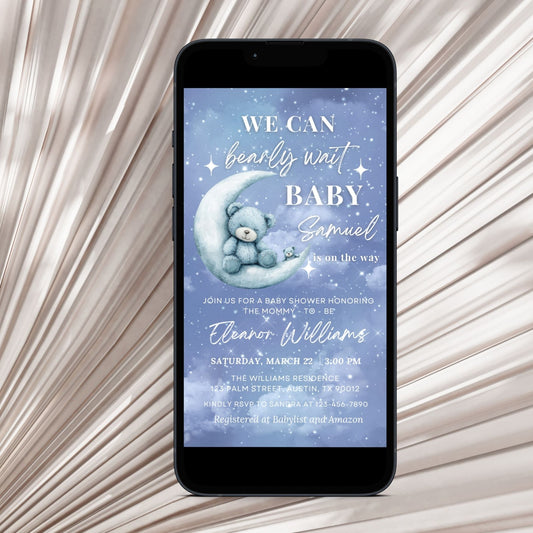 Phone displaying a baby shower invitation with a Cute teddy bear on a moon, on a textured beige background.