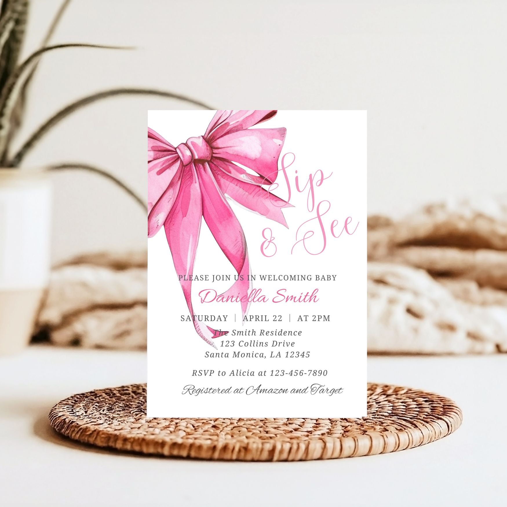 Baby shower invitation with pink bow on a woven mat