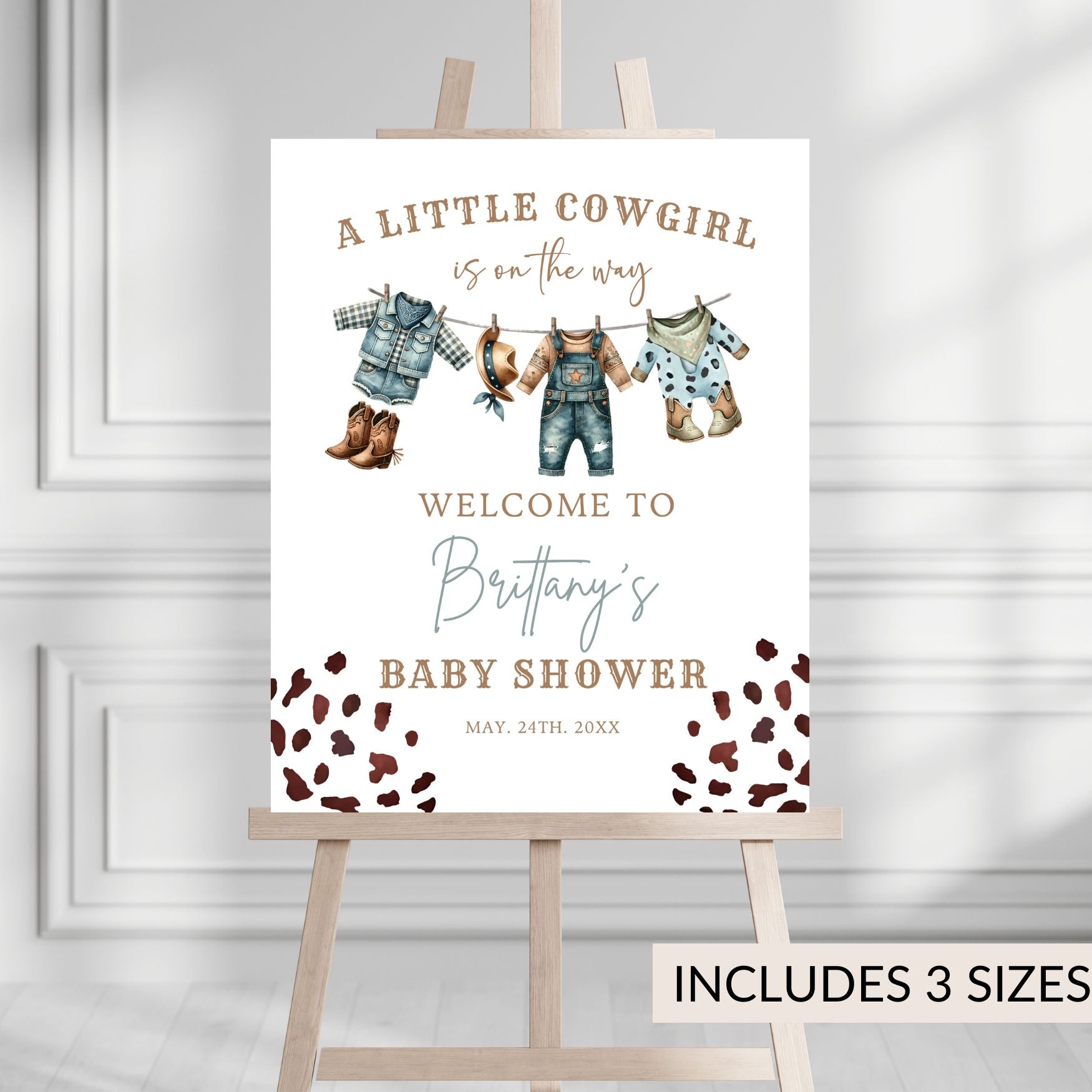 Baby shower sign with cowboy or cowgirl themed elements on an easel against a light gray background.
