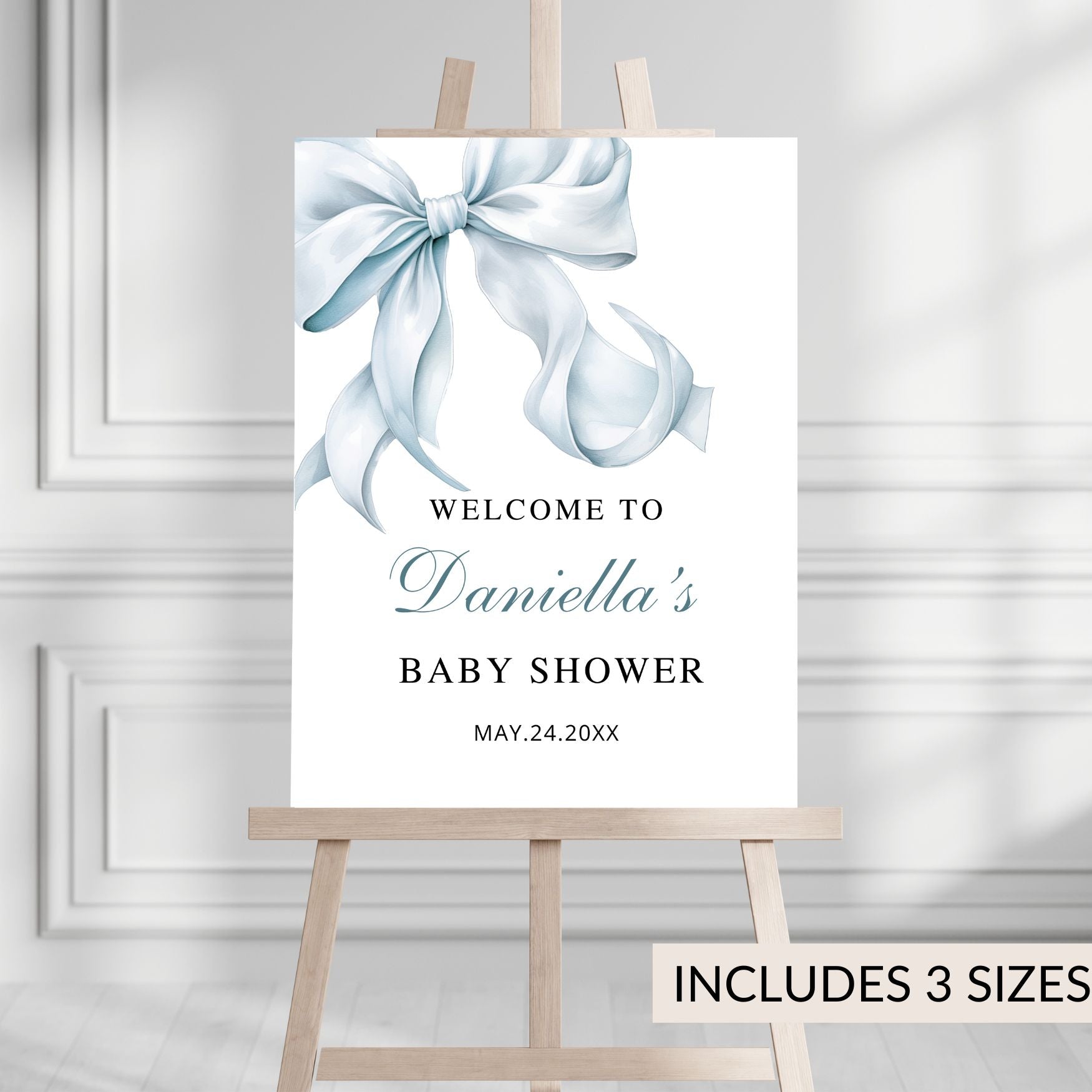 Baby shower welcome sign with a blue bow on a white background, displayed on an easel.