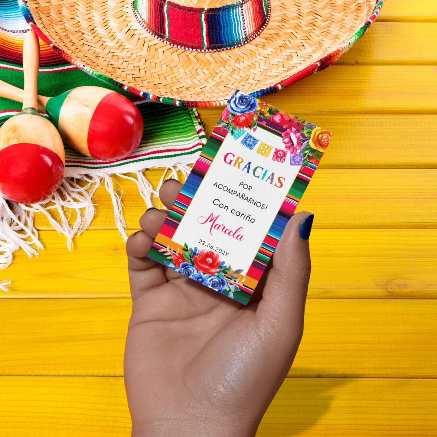 Hand holding a colorful Mexican Fiesta Tag with 'GRACIAS' text, surrounded by maracas and a sombrero on a yellow background.