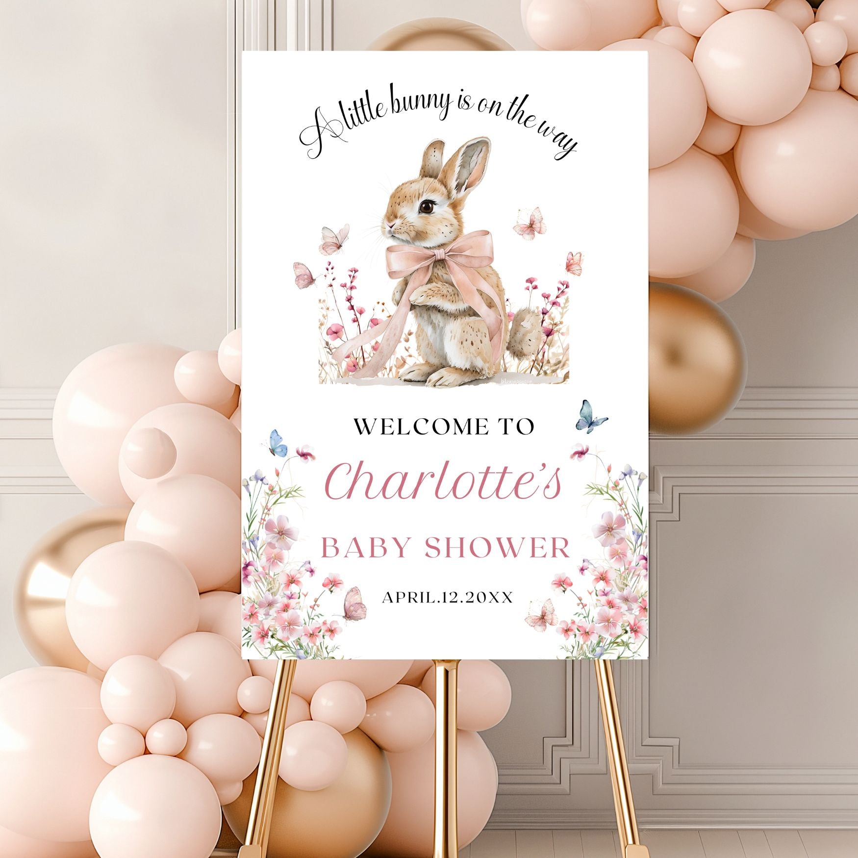 Baby shower sign with a rabbit illustration and wildflowers elements, surrounded by balloons.