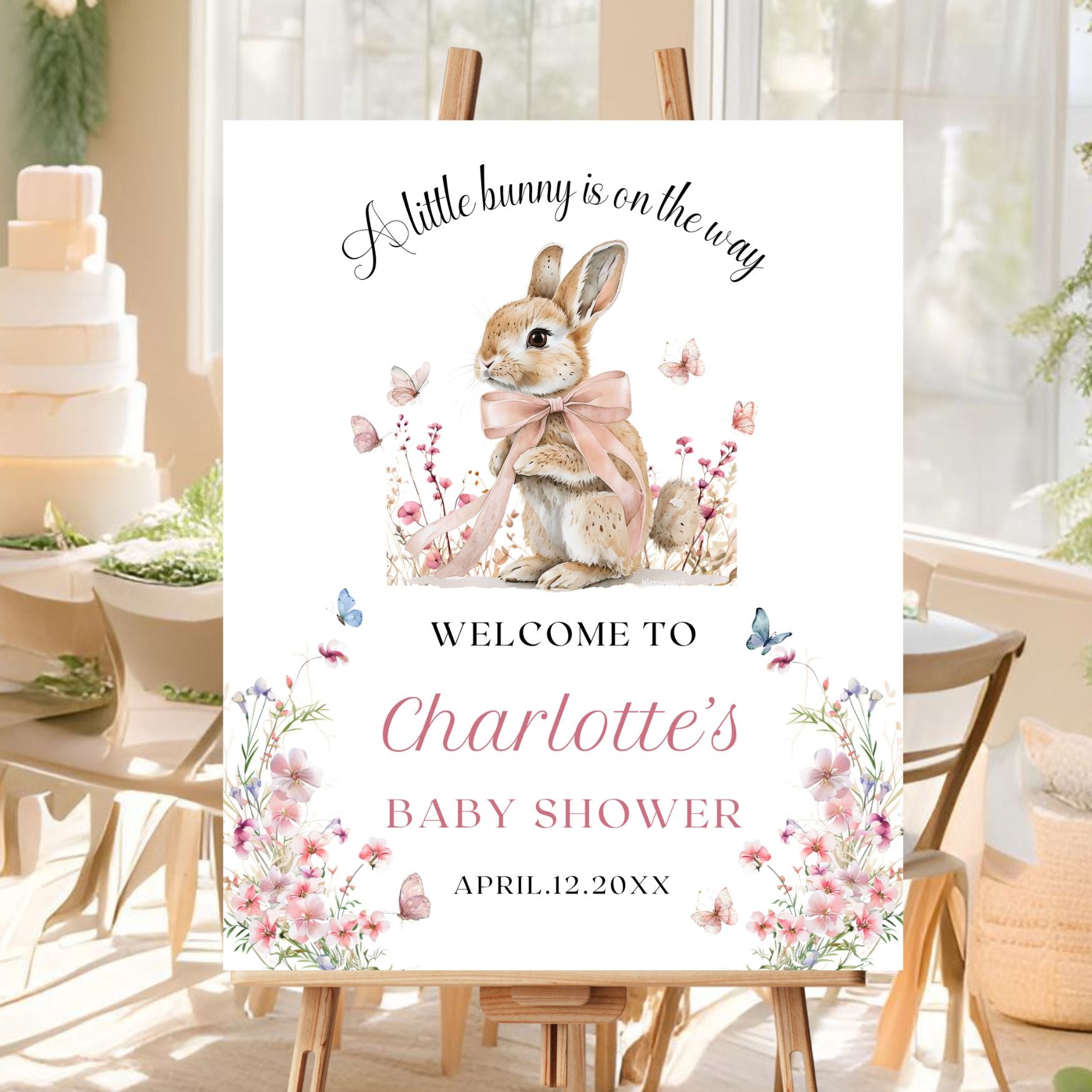 Baby shower sign with a rabbit illustration and floral elements in a decorated room.